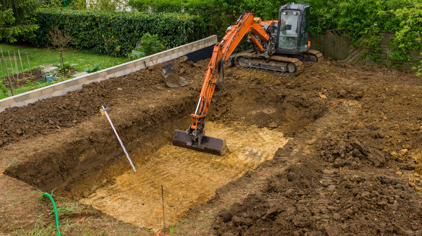 Un jardin résidentiel belge avec une zone délimitée par des piquets et une corde pour marquer l'emplacement futur d'une piscine, un tas de sable visible, terrain nivelé, maison contemporaine en arrière-plan